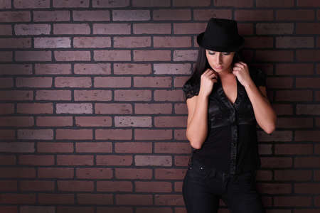beautiful brunette against the wall in a shirt and a hatの写真素材