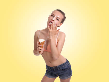 Young beautiful woman eats ice cream in studio , ice cream dripping on the face and breast girl.の写真素材
