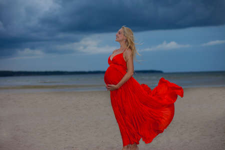 Young positive girl in a red bright dress on a background of cloudy landscapeの写真素材