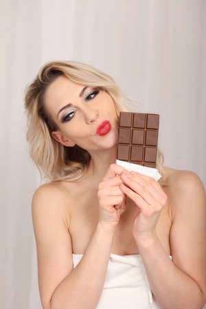 Attractive blonde studio portrait eating chocolate on light backgroundの写真素材