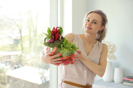 beauty young positive smiling woman with vegetables in the kitchen