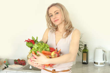 beauty young positive smiling woman with vegetables in the kitchenの写真素材