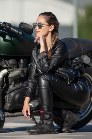 young beautiful woman in black with a motorcycleの写真素材