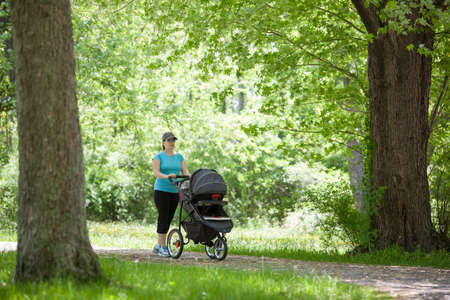 Young mother pushing a stroller in the parkの写真素材