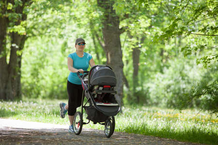Young mother running while pushing a stroller in the parkの写真素材