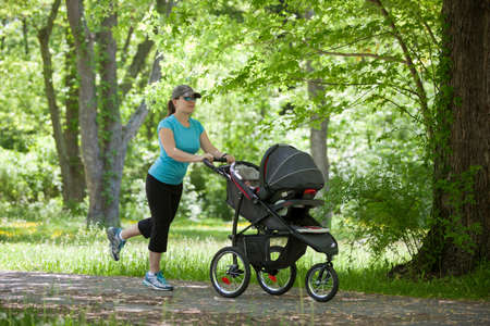 Young mother running while pushing a stroller in the parkの写真素材