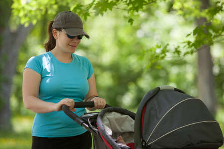 Young mother standing with stroller in the parkの写真素材