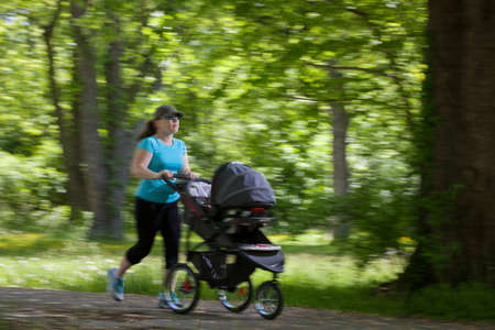 Young mother running while pushing a stroller in the park, panningの写真素材