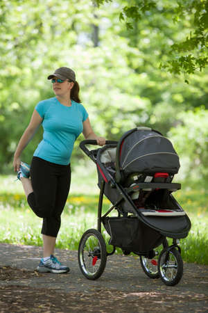 Young woman stretching next to stroller in the parkの写真素材