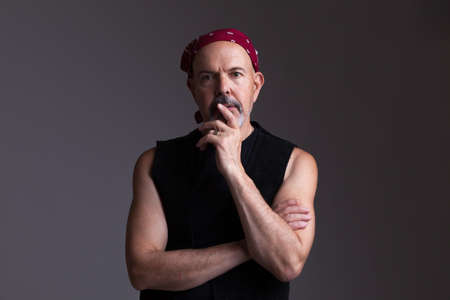 Mature biker in red bandana  fold his hands, serious look, thinking