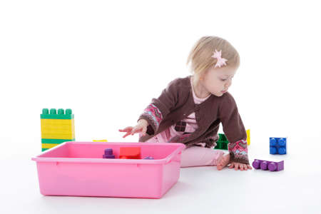 toddler girl picking up toys in pink bin, isolated on white backgroundの写真素材
