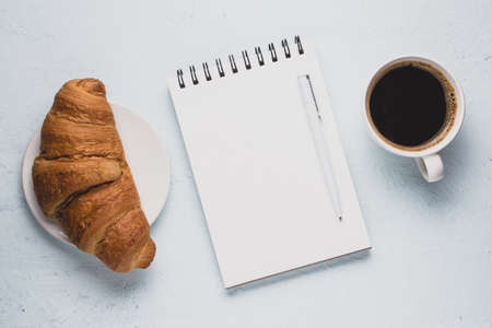 Coffee, croissant and a notepad on a light background. Breakfast conceptの写真素材