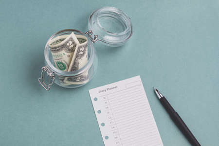 Two dollars in the jar and diary planner on a green background. Savings money or planning conceptの写真素材