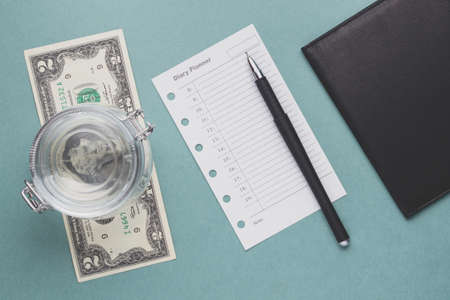 Two dollars and a diary planner on a green background. Flat lay and top viewの写真素材