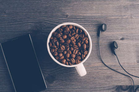 Cup with coffee grains and gadgets on dark wooden background