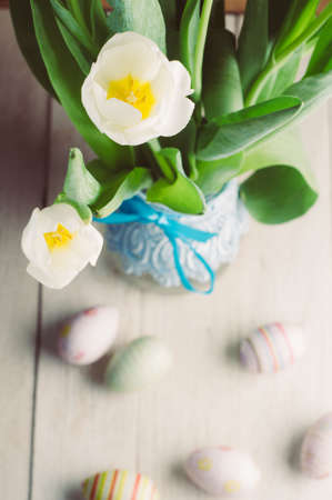 White tulips and Easter eggs on white wooden background. The concept of Easter or spring