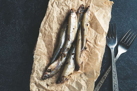 Salted sprat and forks on paper over dark stone background. Copy space for text or designの写真素材
