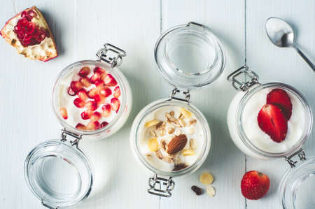 Homemade yogurt in glass jars, dry mix, pomegranate and strawberries over white wooden backgroundの写真素材