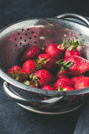 Fresh strawberries in a metal sieve over dark concrete background. Vertical frameの写真素材