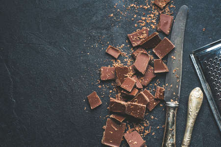 The chunks of chocolate and antique knives over dark concrete backgroundの写真素材