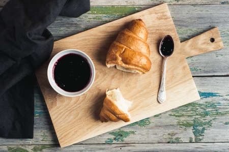 Jam and croissant on a cutting board over old wooden backgroundの写真素材