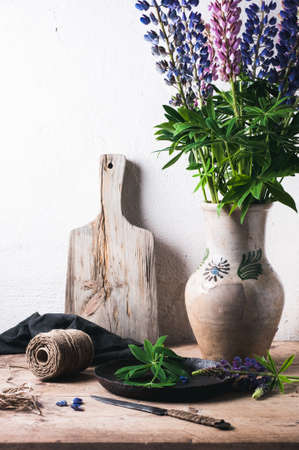 Bouquet of lupines in a clay jug on a wooden table. Concept of the villageの写真素材