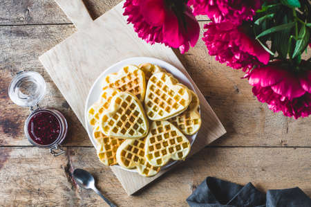 Homemade wafers, raspberry jam and bouquet of red peonies on a wooden tableの写真素材