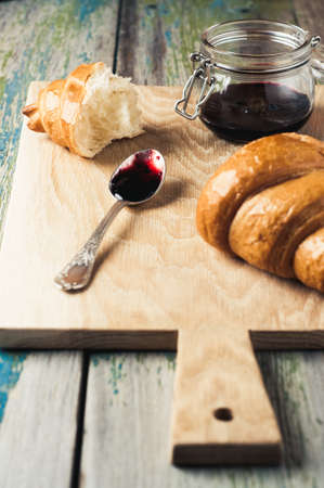 Jam and croissant on a cutting board over old wooden backgroundの写真素材
