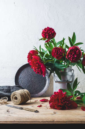 Bouquet of red peonies in a can on a wooden table against the background of a white wallの写真素材