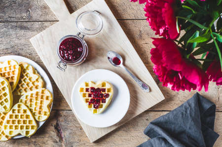 Homemade wafers, raspberry jam and bouquet of red peonies on a wooden tableの写真素材