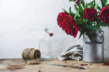 Bouquet of red peonies in a can on a wooden table against the background of a white wallの写真素材
