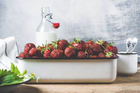 Fresh strawberries in a metal tray and a bottle of milk on old wooden backgroundの写真素材