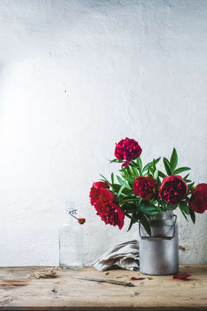 Bouquet of red peonies in a can on a wooden table against the background of a white wallの写真素材