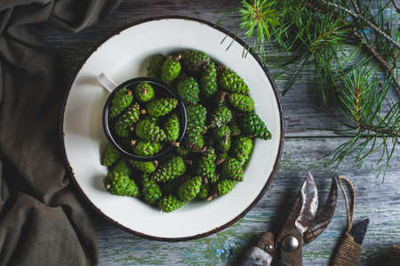 Fresh, green pine cones in a white metal plate on an old wooden tableの写真素材