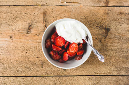 A bowl of yogurt and fresh strawberries on old wooden tableの写真素材
