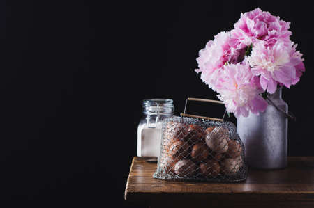 Concept of rural kitchen. Peonies in a can, flour and eggs on a wooden table against the background of a black wallの写真素材