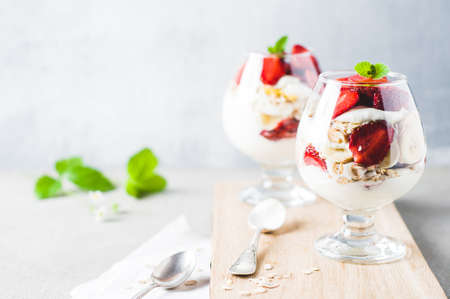 Strawberries and cream in the glass and muesli on cutting board over grey concrete background. Breakfast or natural eating conceptの写真素材