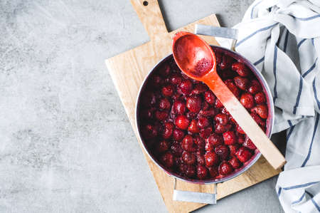 Homemade strawberry jam in an alluminium pan on a grey concrete background