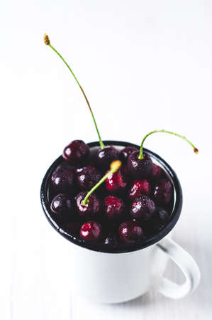 Fresh cherries in a white metal Cup isolated on white backgroundの写真素材