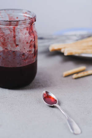 Homemade strawberry jam in jar and snacks on a grey concrete background