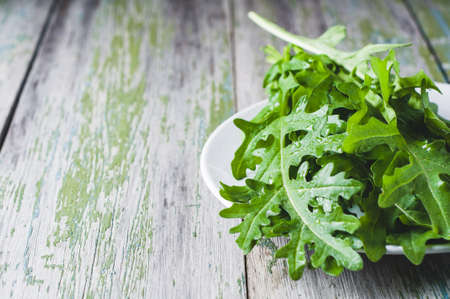 Fresh arugula on a white plate over old wooden backgroundの写真素材