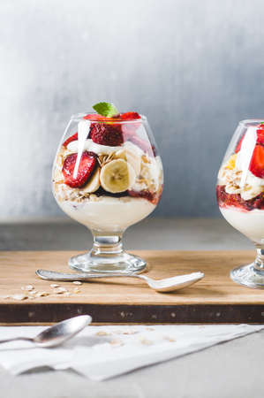 Strawberries and cream in the glass and muesli on cutting board over grey concrete background. Breakfast or natural eating conceptの写真素材