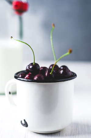 Fresh cherries in a white metal Cup and bottle of milk on white background