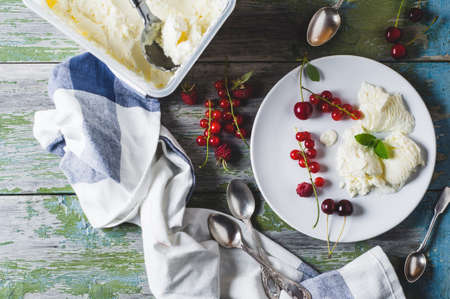 Homemade ice cream with red currants and berries on a plate over old wooden tableの写真素材
