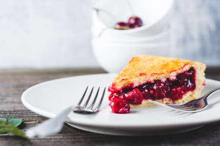 Cherry pie and fresh berries in a bowl on a dark wooden table