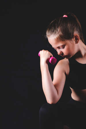 Young fitness girl with dumbbells on black background. Sport or  healthy lifestyle conceptの写真素材