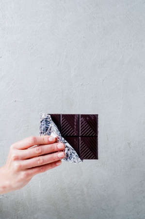 A bar of chocolate in a female hand on a gray backgroundの写真素材