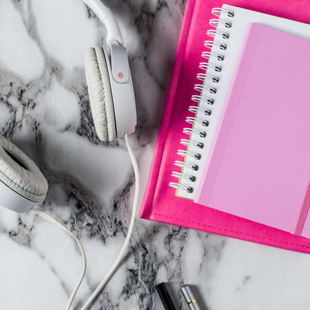 White headphones and a pink notebook on the marble background