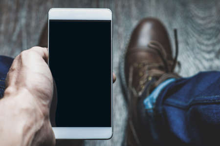 A young man takes pictures of his shoes on a mobile phone. Point of viewの写真素材