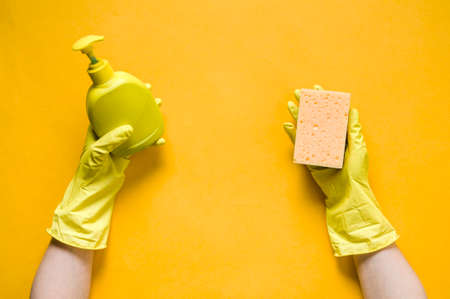 Hands in yellow gloves holding sponge and detergent. The concept of cleaning or washing dishesの写真素材